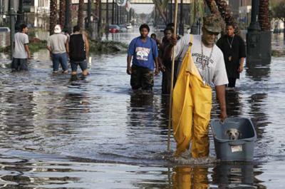 People walking through water after Hurricane Katrina. One person in the foreground is carrying a bin with a small dog in it