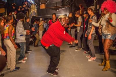 A person in a red shirt dances while surrounded by other people.
