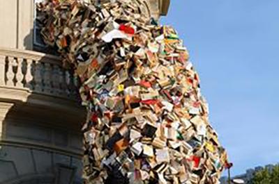 A sculptural installation by Alicia Martin at Casa de America, Madrid, of a wave made of thousands of books falling from a second-story window to the ground.