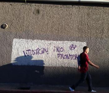 A man walks alongside a wall that has writing on it reading justice and no border in Spanish.