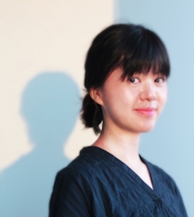 Profile image of Ying-Hsiu Chou in a dark blue top against a white wall with blue shadows. Her hair is dark and pulled back in a low bun with bangs in front. She is smiling close-lipped at the camera.