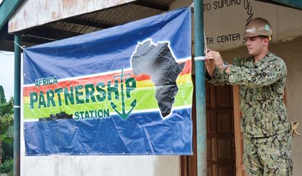 US Navy sailor in uniform secures a banner with a silhouette of Africa and text that reads: “Africa Partnership Station”