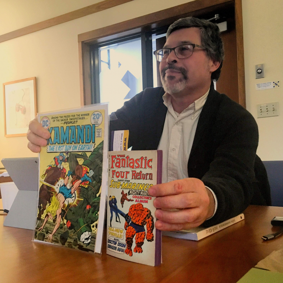 José Alaniz sits at a table holding two comic books.
