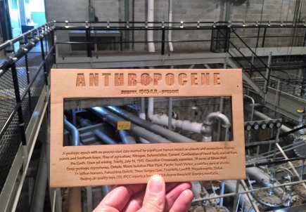 A hand holding Smudge Studio’s Anthropocene Viewer in front of pipes in the B Reactor interior