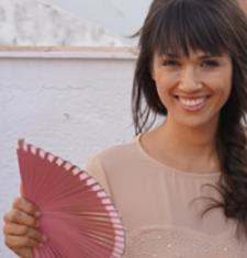 Angela Durán Real holds a pink fan while standing in front of water.
