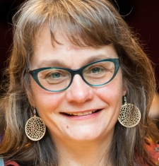 Portrait of Lynn Thomas wearing glasses and yellow dangle earrings.