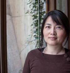 Ping Wang stands in front of a window wearing a brown shirt.