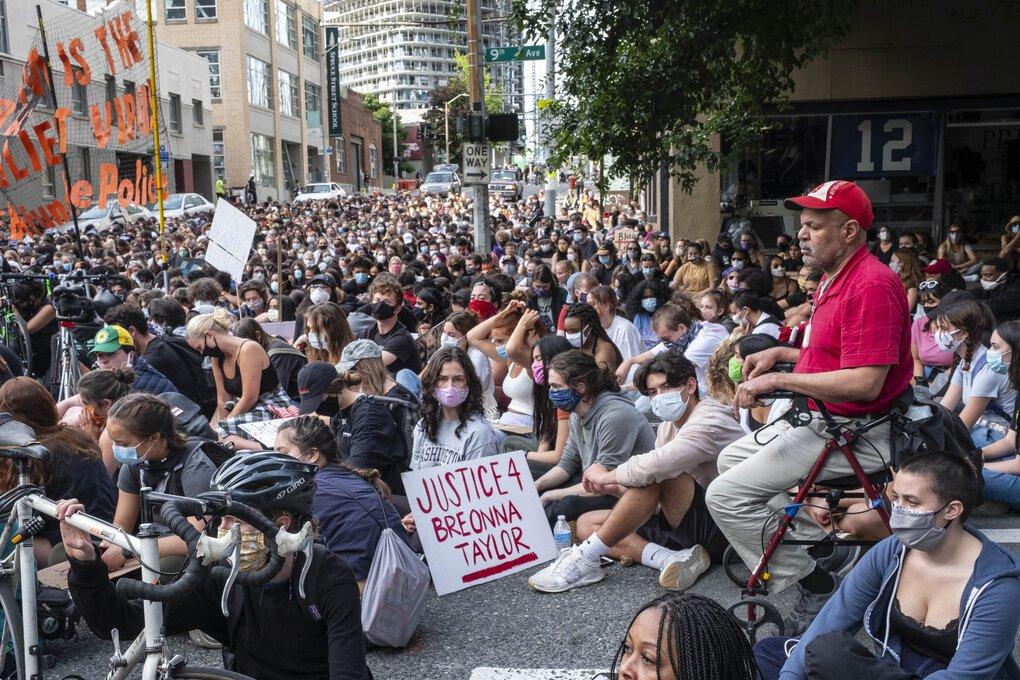 Protesters participating n the Seattle Youth Protest sit in the intersection outside the Seattle Police Department. One protester holds a sign reading, "Justice 4 Breonna Taylor"