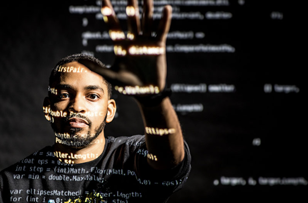 african american male-presenting profile reaching toward the camera with TEI coding projected across his face and hands