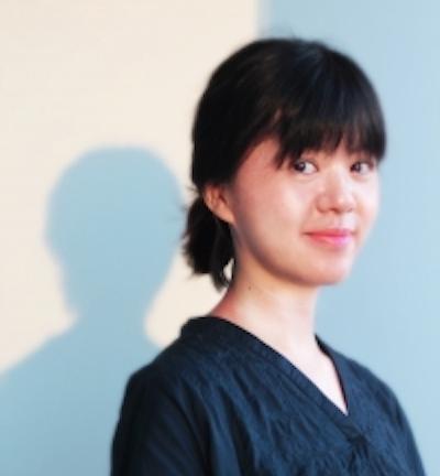 Profile image of Ying-Hsiu Chou in a dark blue top against a white wall with blue shadows. Her hair is dark and pulled back in a low bun with bangs in front. She is smiling close-lipped at the camera.