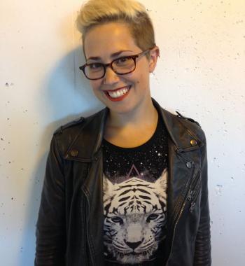 AJ smiles while wearing dark glasses a black shirt with a white tiger on it and a black jacket while standing in front of a white background.