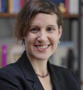 Mika Ahuvia in suit jacket smiling with bookcase in background 