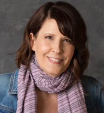 Portrait of Christine Harold wearing a purple scarf and sitting in front of a dark wall.