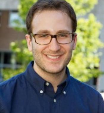 Portrait of Daniel Bessner in a blue shirt and glasses