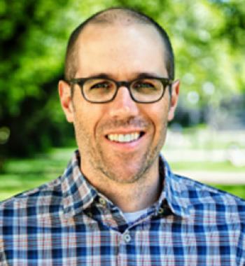 Portrait of Ian Schnee wearing glasses and standing outside.