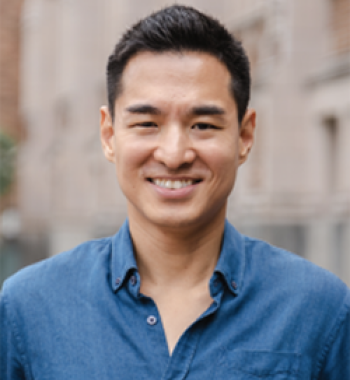 Jang Wook Huh stands outside in front of a building wearing a blue shirt.