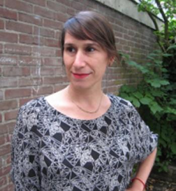 Jenna Grant stands outside in front of a brick wall wearing a patterned shirt. 