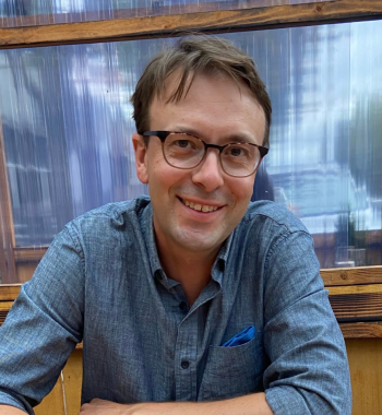 A close-up image of Jesse Oak Taylor wearing a blue shirt and glasses.