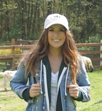 Jessica Holmes stands outside wearing white cap and denim jacket.