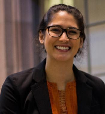 Profile of Katia smiling at the camera in a dark blazer and orange shirt