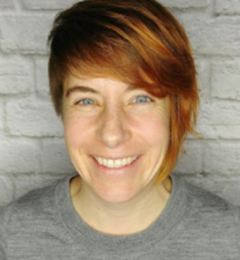 Laurie Marhoefer stands in front of a white brick wall wearing a grey shirt.