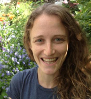 Lily Shapiro stands in front of a bush wearing a blue shirt.