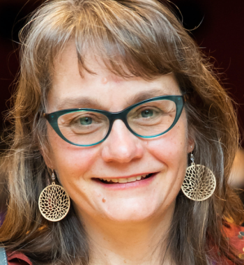 Portrait of Lynn Thomas wearing glasses and yellow dangle earrings.
