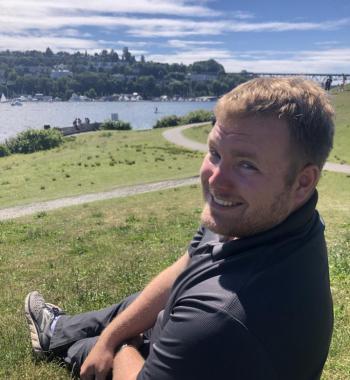 Matthew Childs sits outside on a hill overlooking a body of water.