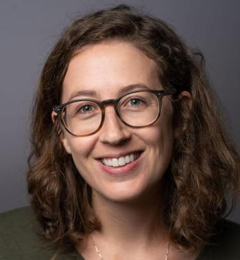 Headshot of Melanie Walsh standing in front of a grey wall wearing glasses.