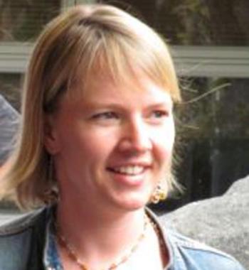 Janice Moskalik looks to the right and smiles while wearing a light shirt and denim jacket.