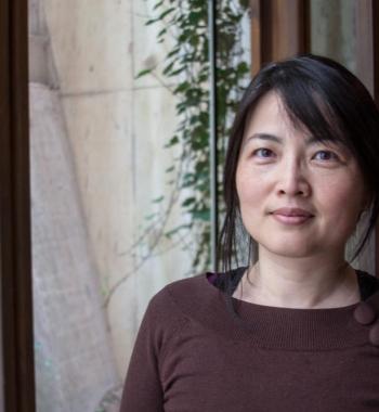 Ping Wang stands in front of a window wearing a brown shirt.