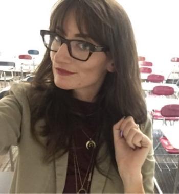Photo of Alexandra Meany looking to the left while wearing glasses and a tan jacket