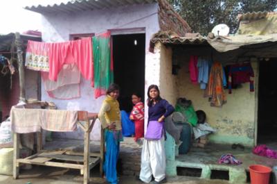 Three women sit or stand near a building's doorway with colorful laundry hanging around them.