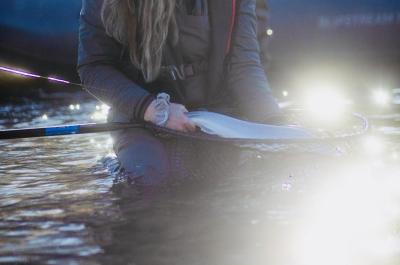 A figure sitting in water holds a fish inside of a net. The water is reflecting the sun