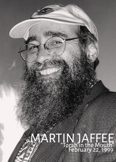 A black and white picture of Martin Jaffee looking into the camera while smiling and wearing a baseball cap and glasses.