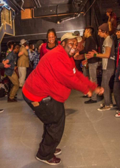 A person in a red shirt dances while surrounded by other people