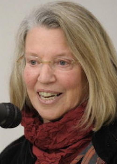 Close-up image of Nancy Fraser speaking into a microphone while wearing glasses and a red scarf.