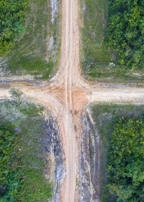 Aerial view of dirt crossroads on green landscape.