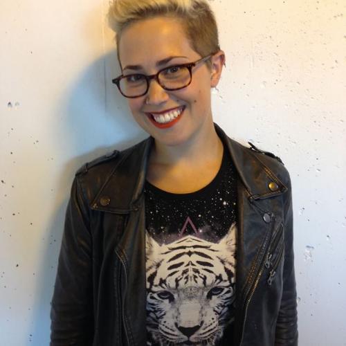 AJ smiles while wearing dark glasses a black shirt with a white tiger on it and a black jacket while standing in front of a white background.