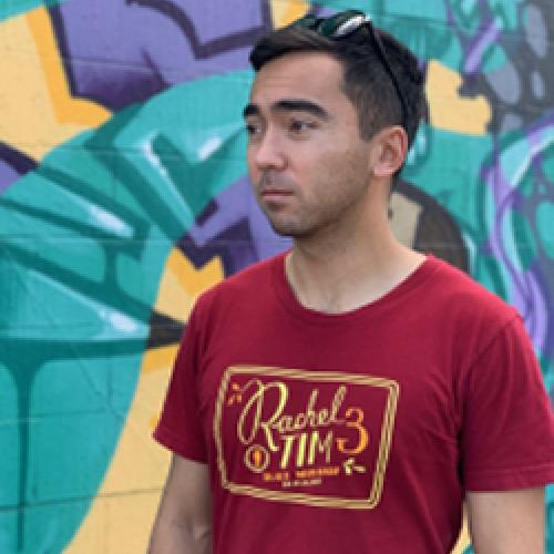 Alika Bourgette wears a red shirt while standing in front of a multicolored wall.