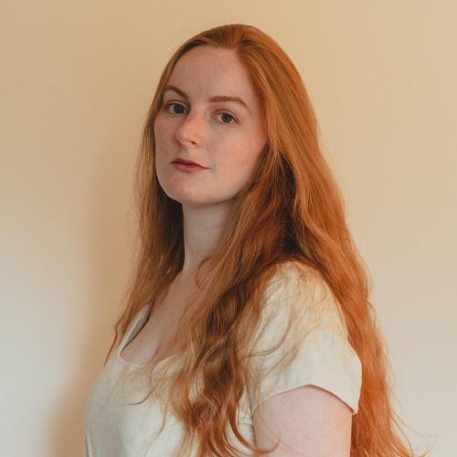 Caitlin looking sideways at the camera. She has long red hair and is wearing a white t-shirt