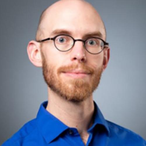 Portrait of Colin Marshall wearing a blue shirt and glasses.