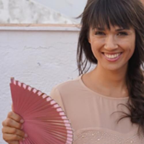 Angela Durán Real holds a pink fan while standing in front of water.