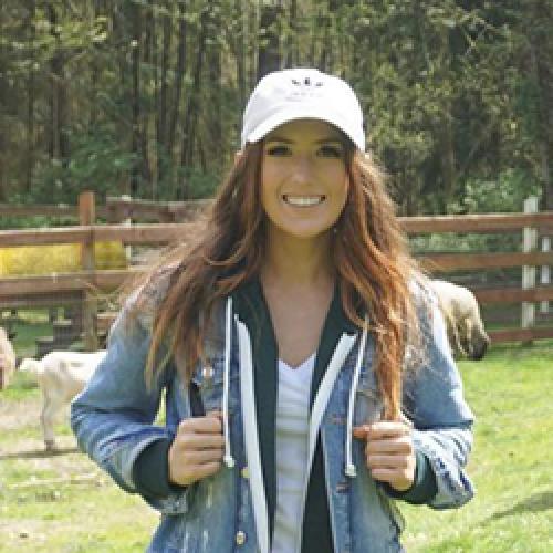 Jessica Holmes stands outside wearing white cap and denim jacket.