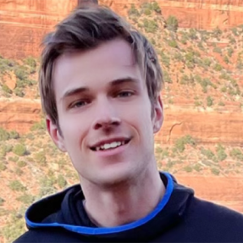 Close-up image of Joe Wilson wearing a sweatshirt while standing in front of a red rock formation.