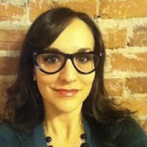 Pamela Pietrucci stands in front of a brick wall wearing glasses an a green shirt.