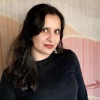 In this photo nanya is wearing a black shirt and standing in front of a beaded curtain and looking at the camera. 