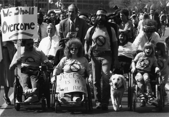 A black and white photo of a group of people walking and in wheelchairs protesting with signs.