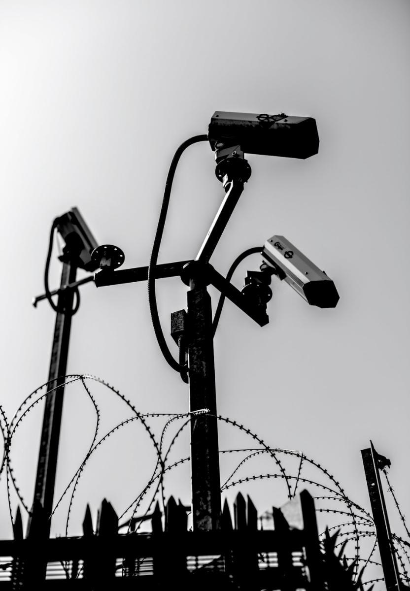 Three surveillance cameras atop barbed wire and spiked poles