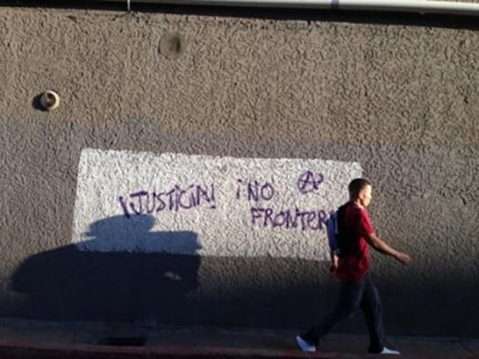 A man walks alongside a wall that has writing on it reading justice and no border in Spanish.
